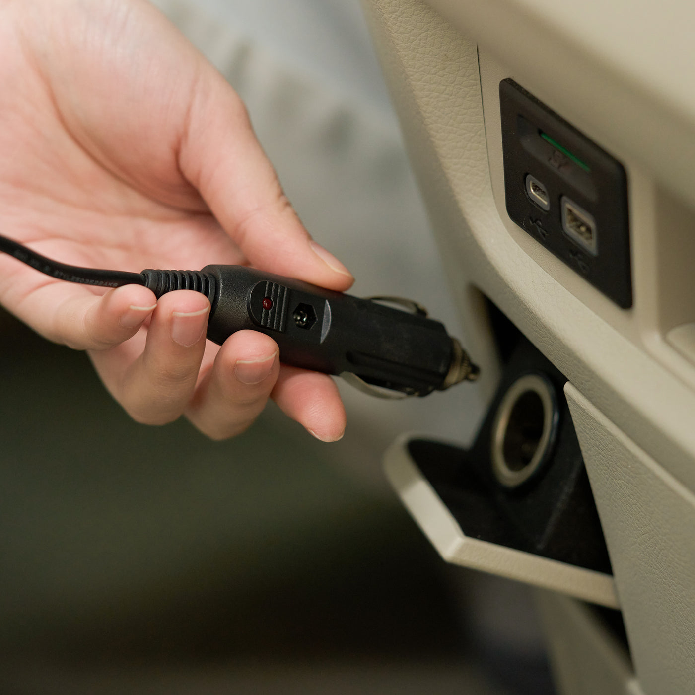 Hand plugging a car charger into a vehicle's USB port.