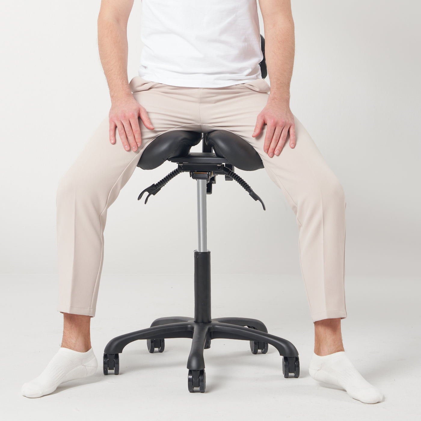 Person sitting on a black saddle-style stool with adjustable height against a white background