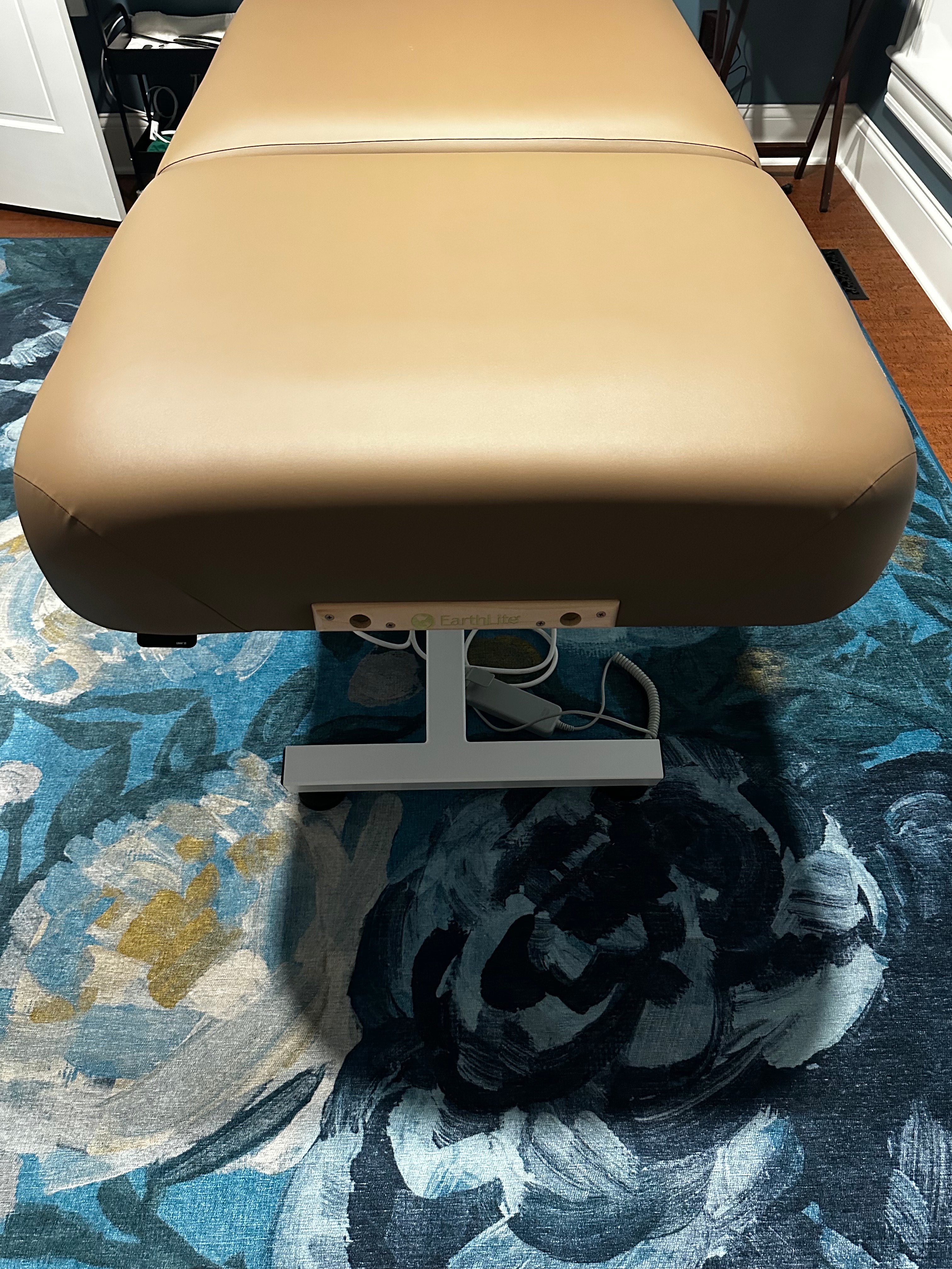 An EarthLite ELLORA TILT brown massage table stands on a floral rug in a cozy room.