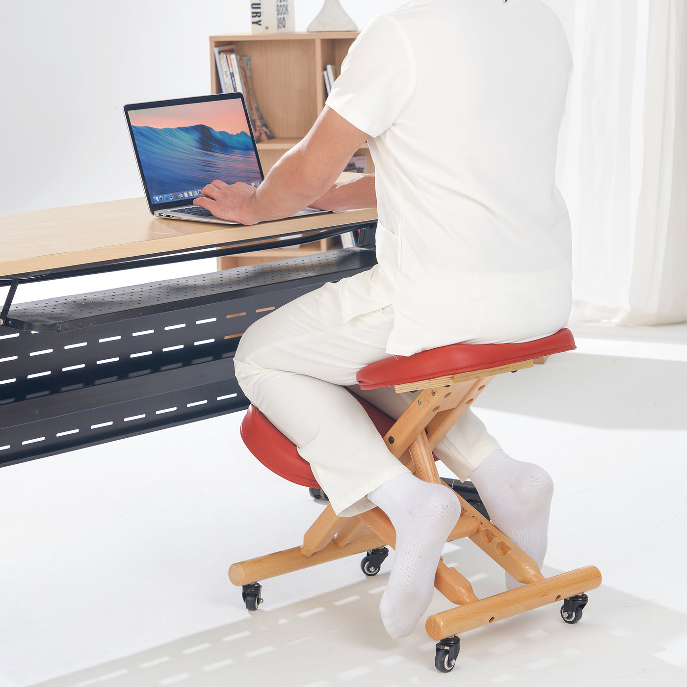 Person using a height-adjustable stool at a desk with a laptop.