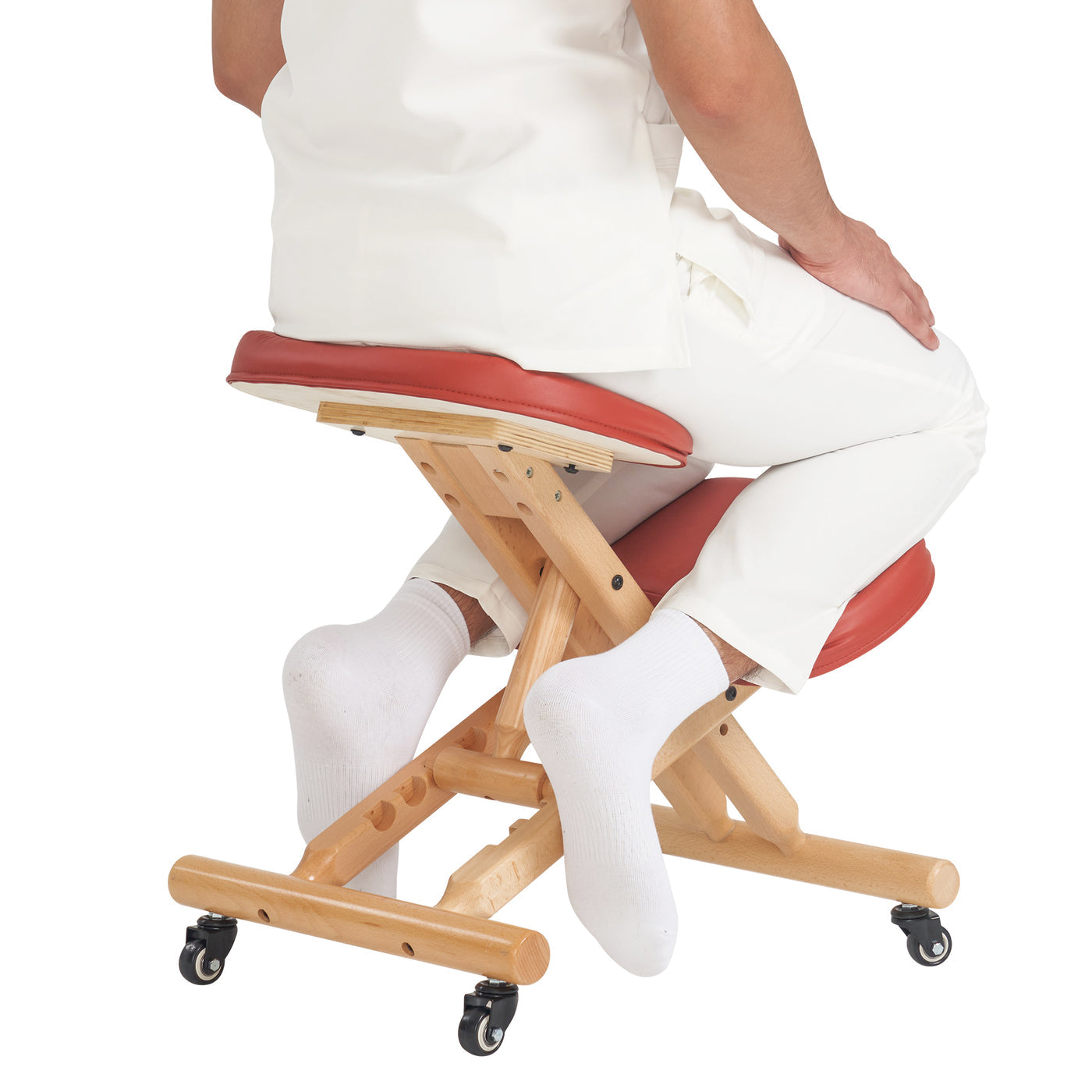Person sitting on a cinnamon and wooden kneeling chair with white pants and socks.