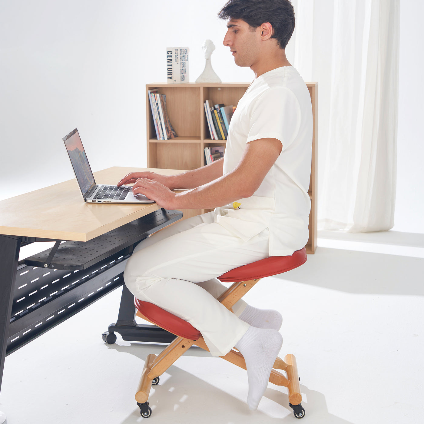 Person sitting on a unique chair at a desk using a laptop in a bright room.