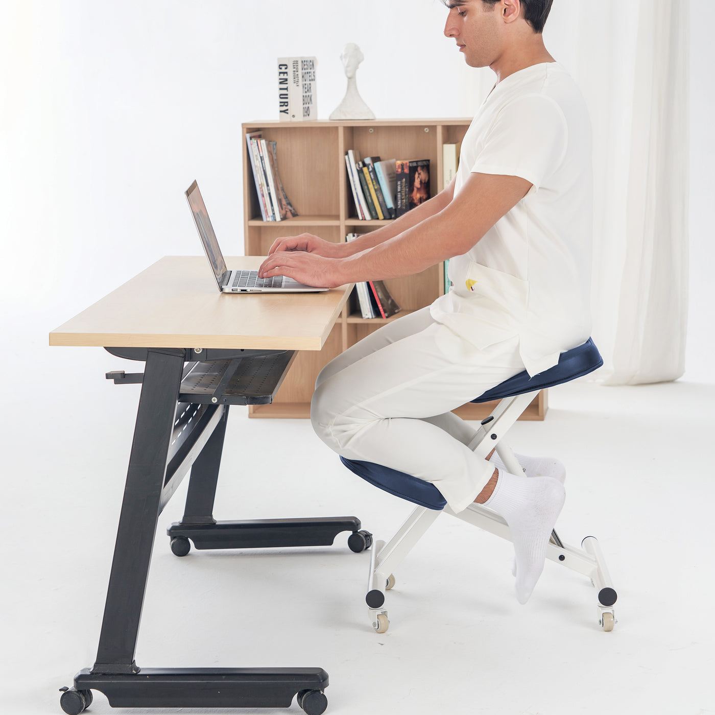 Person using a laptop on a height-adjustable desk with a bookshelf in the background
