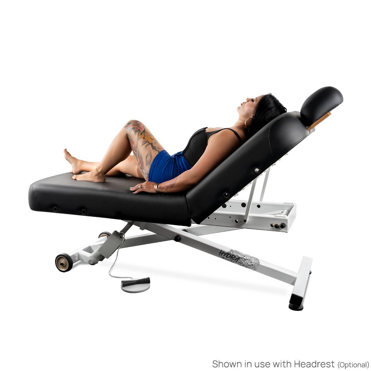 Woman reclining on EarthLite HYDRA Lift Tattoo Table with headrest for artist comfort.