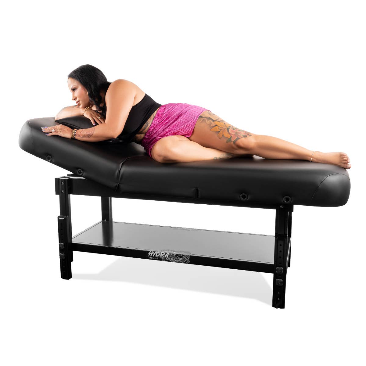 Woman lying on EarthLite HYDRA Stationary Tattoo Table with storage shelf underneath.