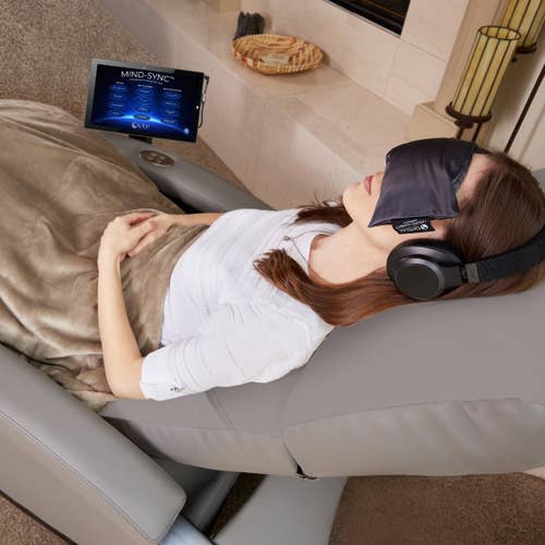 Woman relaxes on Living Earth Crafts Mind-Sync 2.0™ Lounger with headphones, eye mask, tablet.