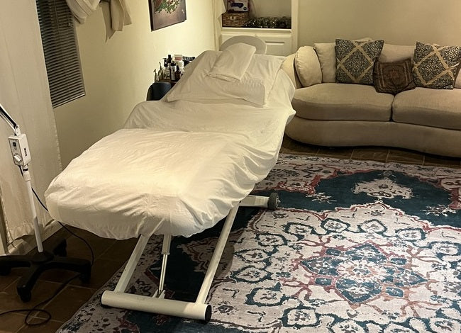 A cozy room with a Silverfox America 2274B Massage Bed, white sheet, sofa, and rug.