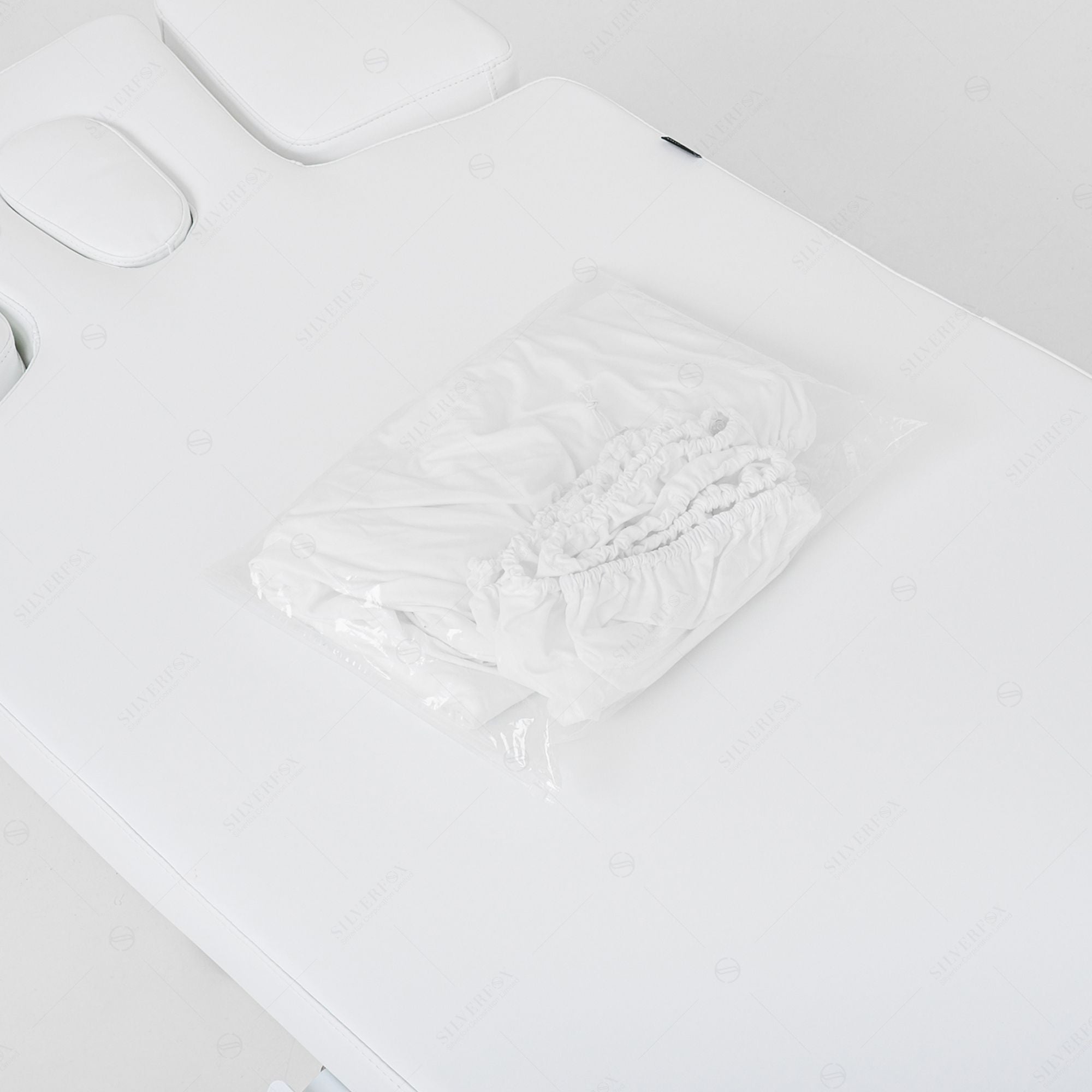 A folded white fitted sheet in plastic on a Silverfox America OCILI 2249 massage table.
