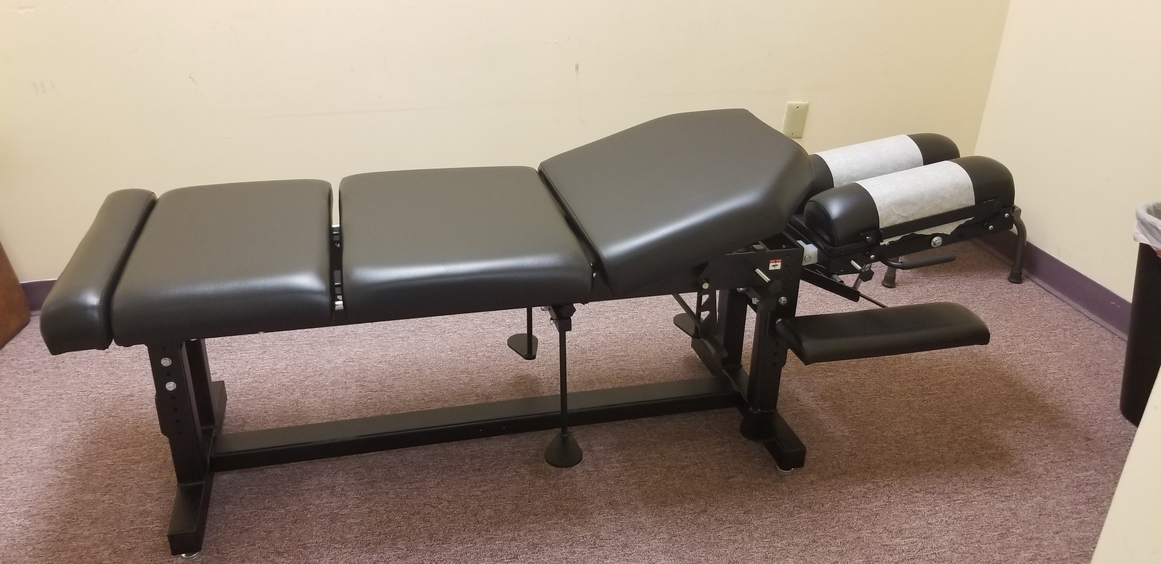 PHS METAL Max Drop Treatment Table by PHS Chiropractic in a small room with beige carpet.