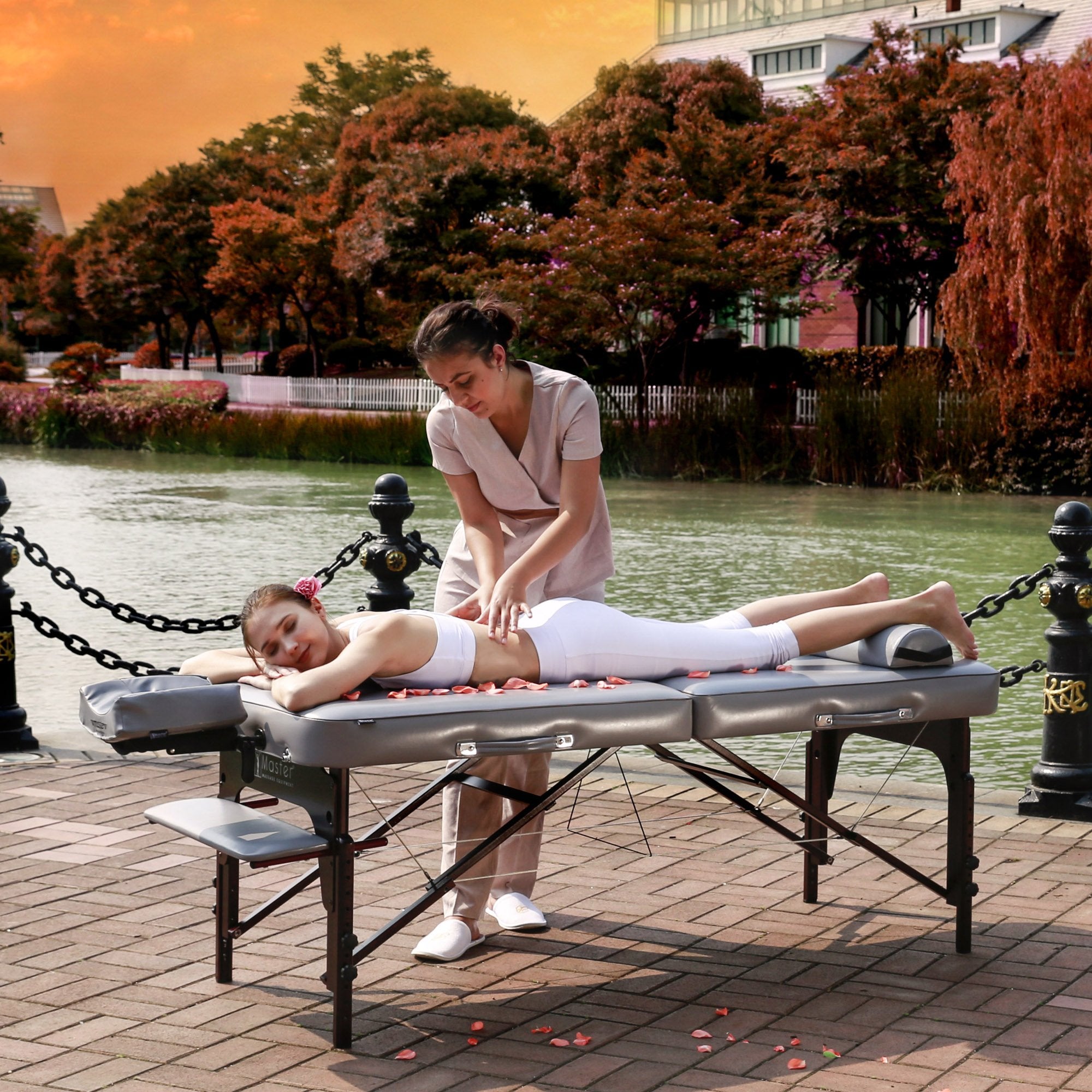 A woman enjoys a massage outdoors on a Master Massage MONTOUR Massage Table by water and trees.