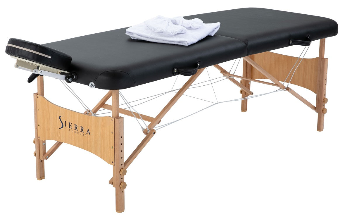 Sierra Comfort ALL-INCLUSIVE portable massage table with wooden legs and folded white sheet.