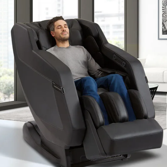 Man relaxing in Sharper Image RELIEVE 3D Massage Chair with L-track in a modern room with windows.