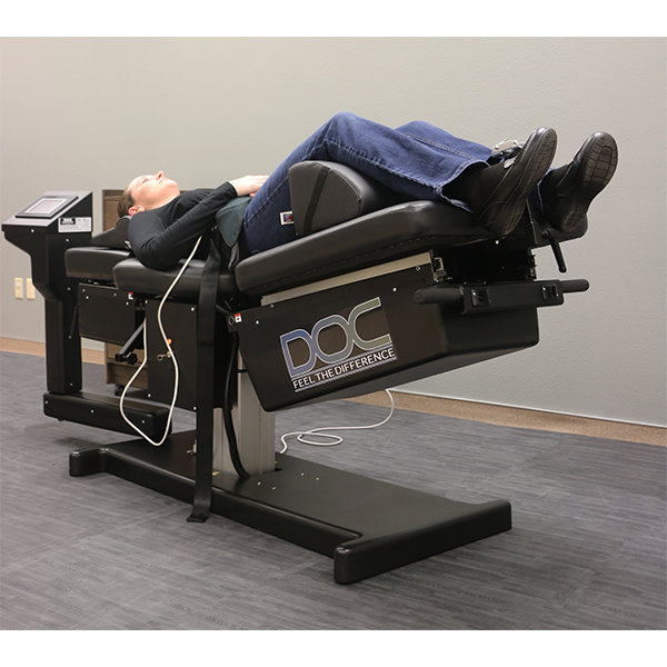 Person lying on a PHS Medical DOC Decompression Table with digital controls in a clinic.
