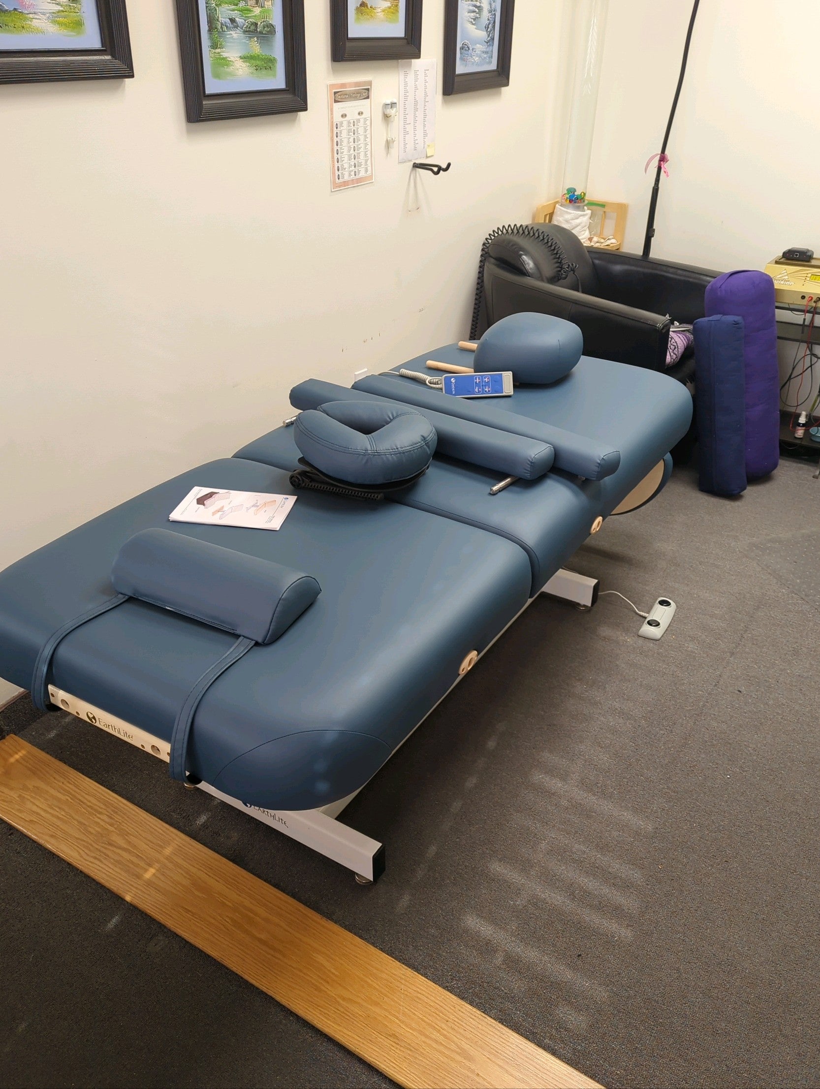 EarthLite EVEREST TILT Lift Massage Table with cushions in a therapy room with framed art.