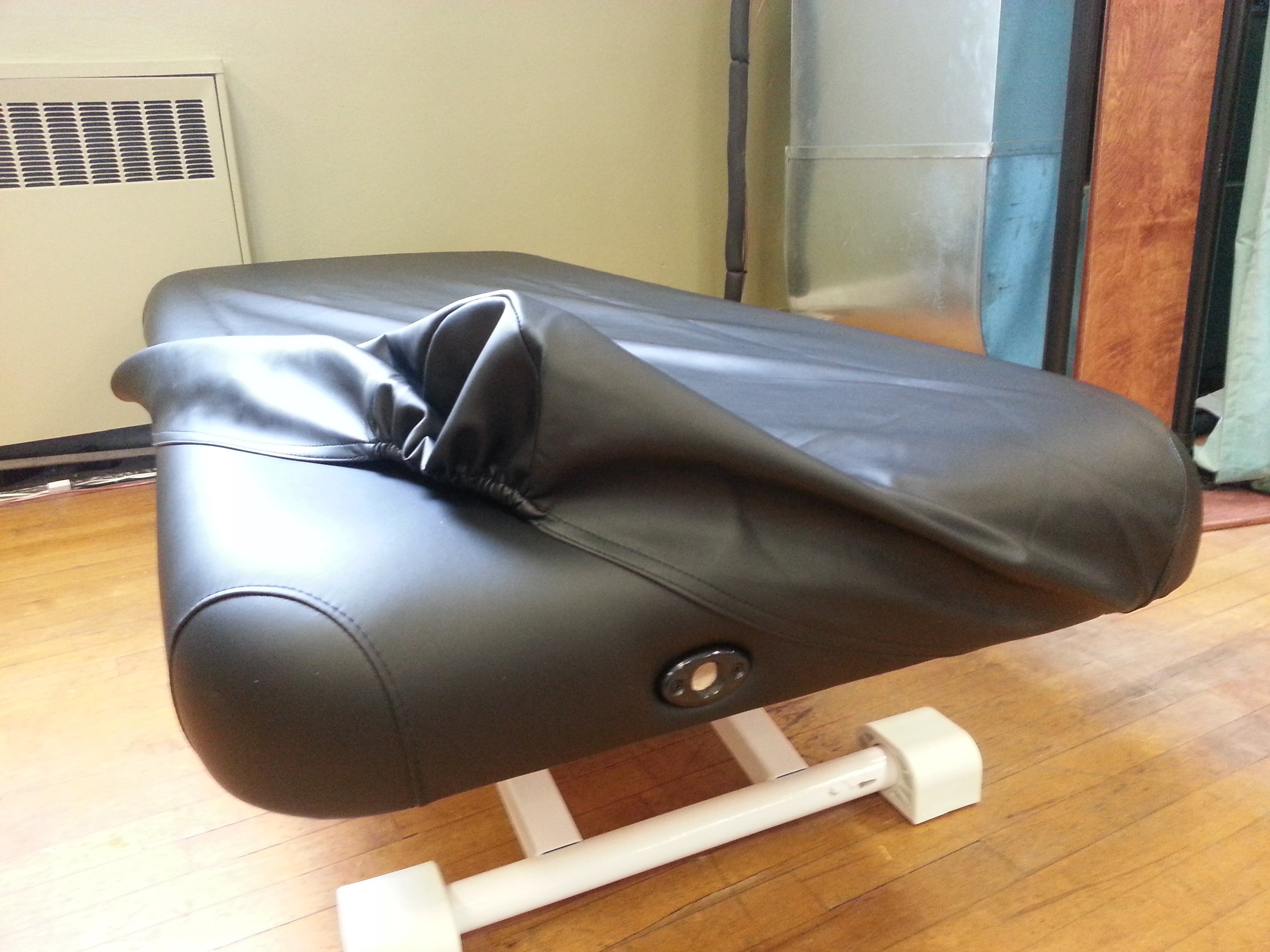 A Nirvana Electric Massage Table with black upholstery is in a room with a wooden floor.
