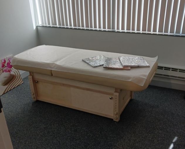 Exam room with window blinds, EarthLite SEDONA TILT massage table, and paper cover.