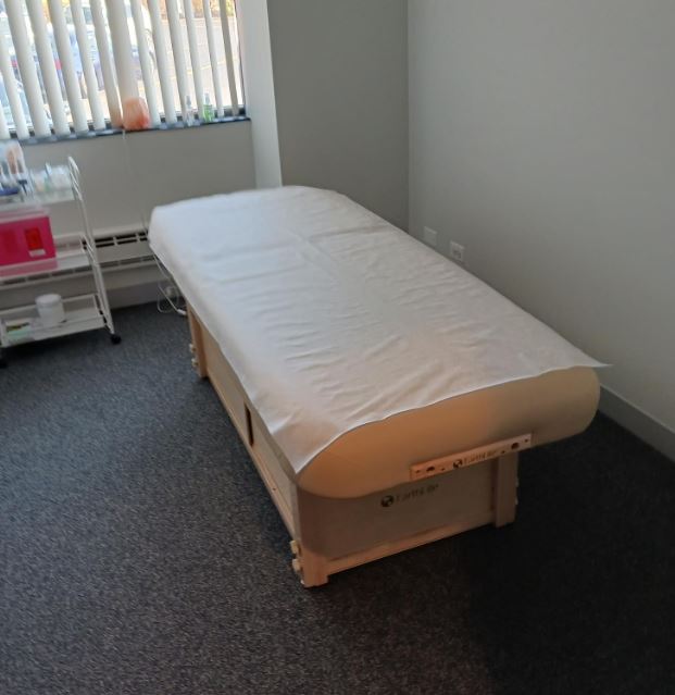 An EarthLite SEDONA TILT table with a paper cover in a small, bright treatment room.