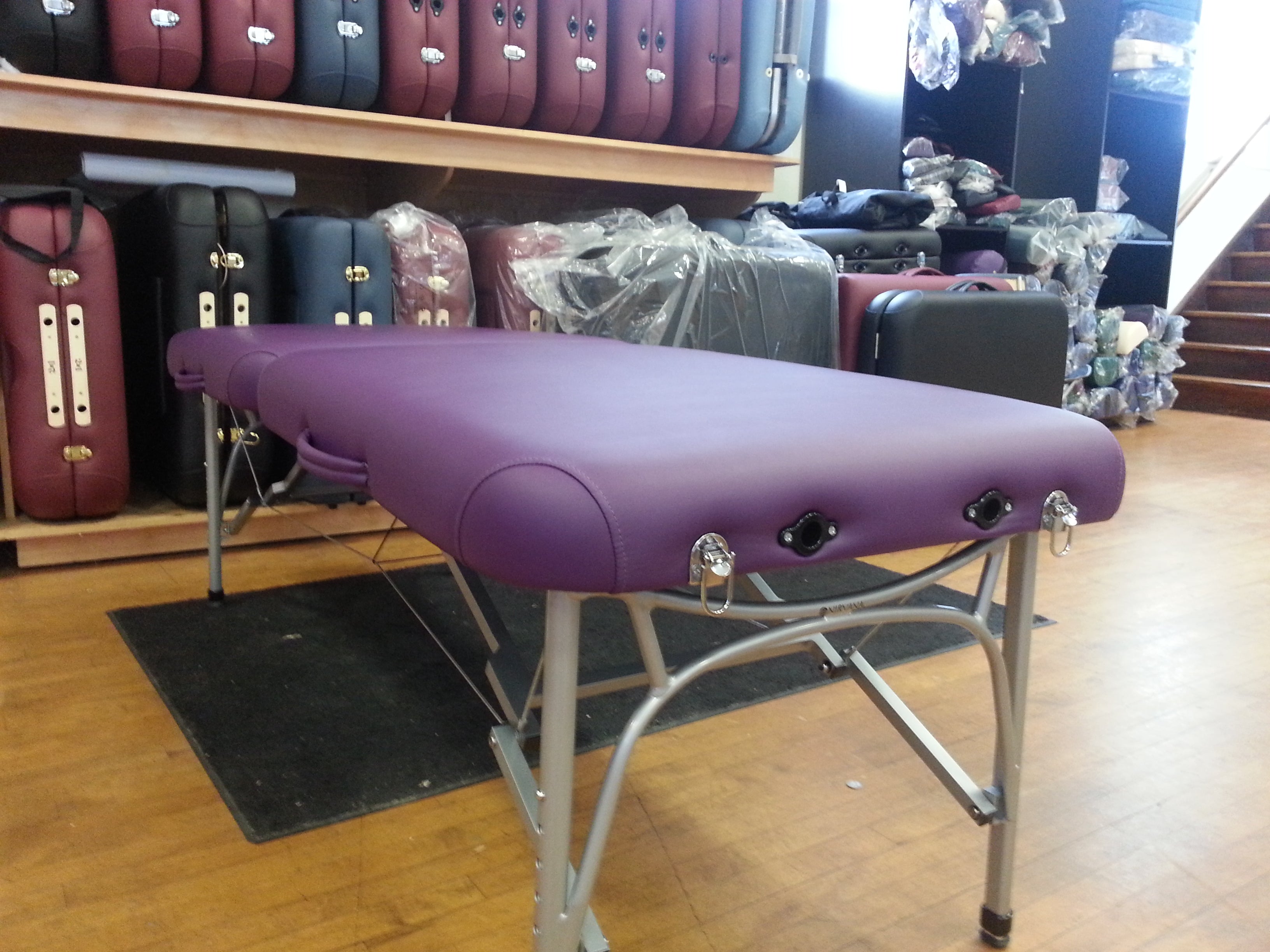 A Nirvana DHARMA SuperLite purple massage table is displayed in-store with others stacked behind.
