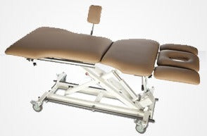 Armedica AM-BAX 5600 pelvic health table with elevating center and brown padded legrest on wheels.