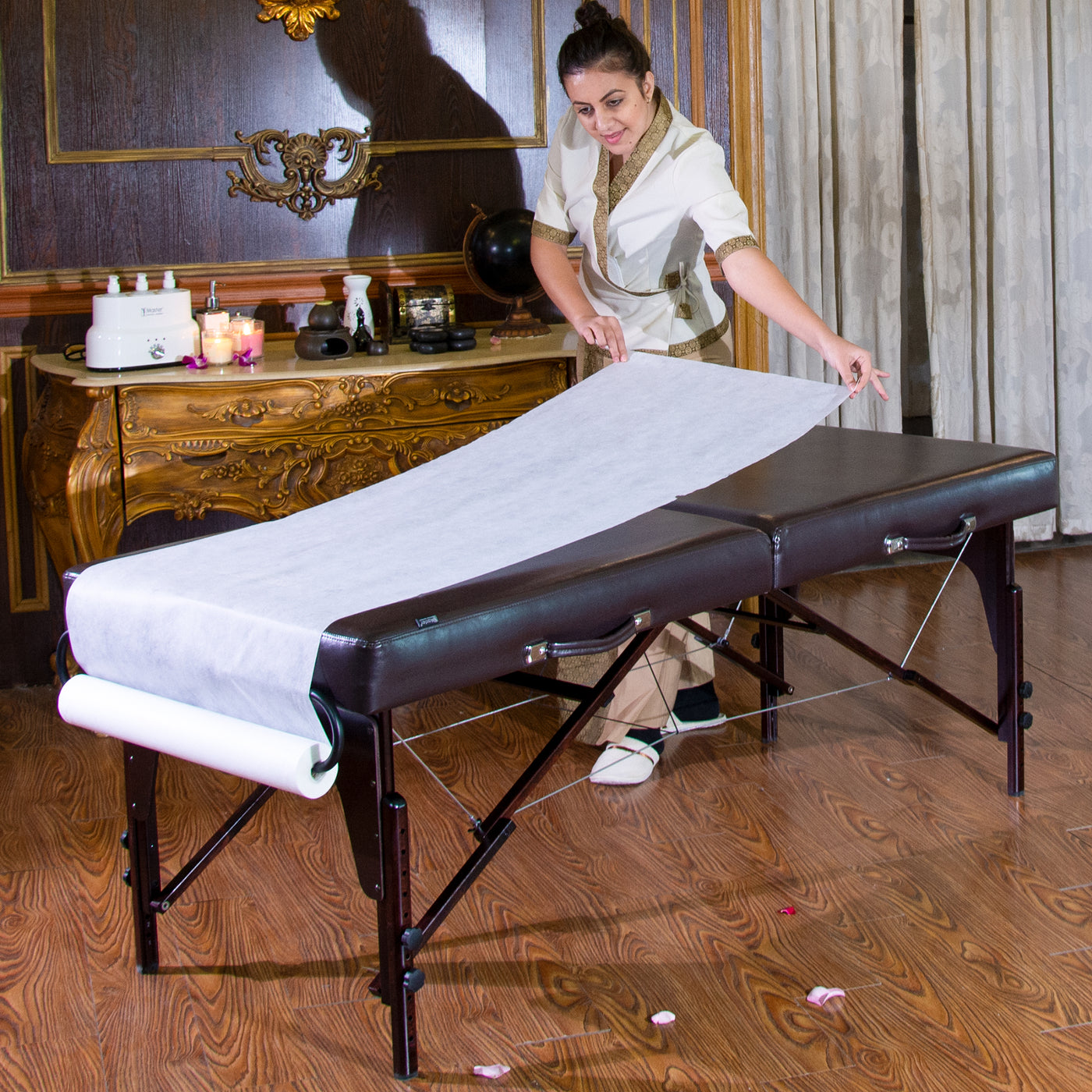 Woman setting up Master Massage Disposable NON-WOVEN Roll with wooden floor and decorative elements.