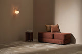 Brown Ceragem S4 Massage Lounger with cushions in a dimly lit room with a wall lamp.