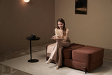 Woman sitting on a brown Ceragem S4 Massage Lounger in a dimly lit room.