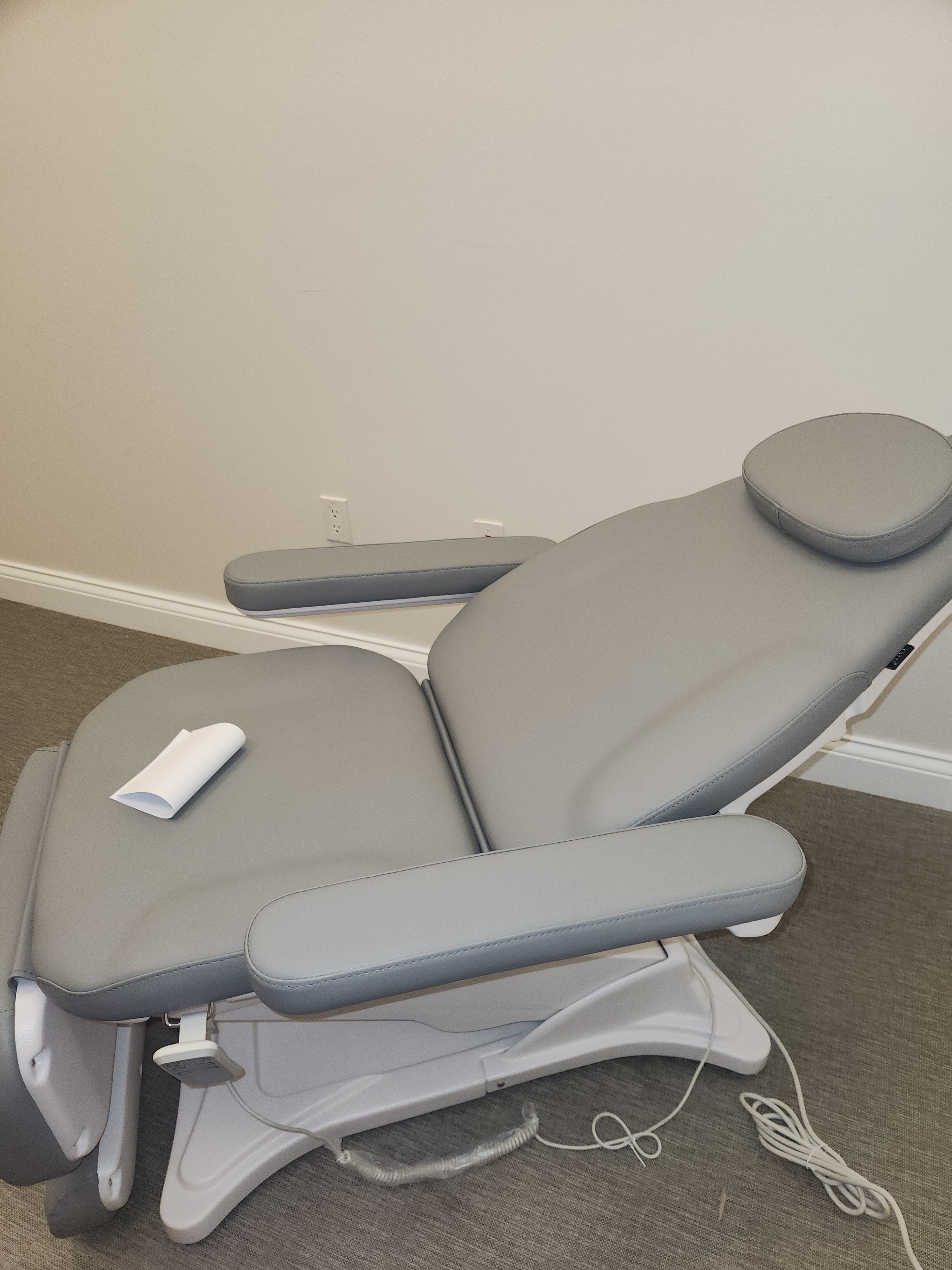 DIR Bellucci Electrical Facial Bed in gray with seat paper, set up in a clinical room.