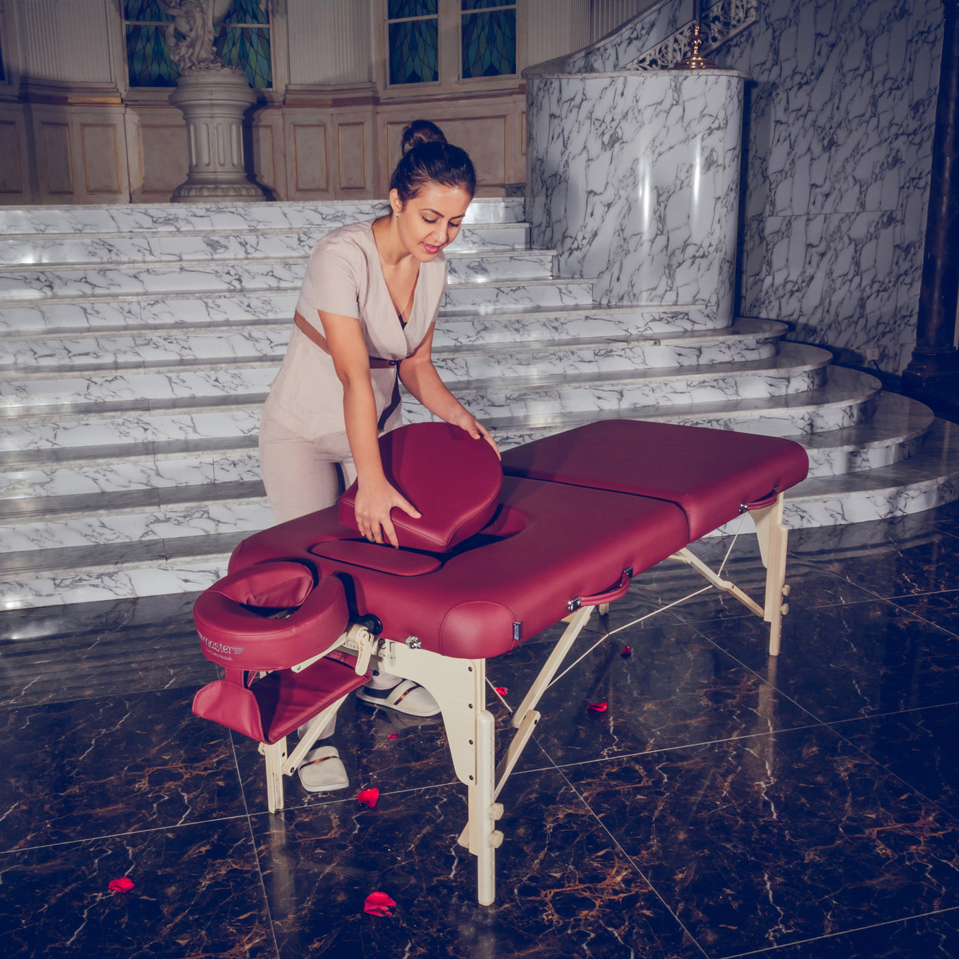 A woman sets up a Master Massage EVA PREGNANCY table with a red cover before marble stairs.
