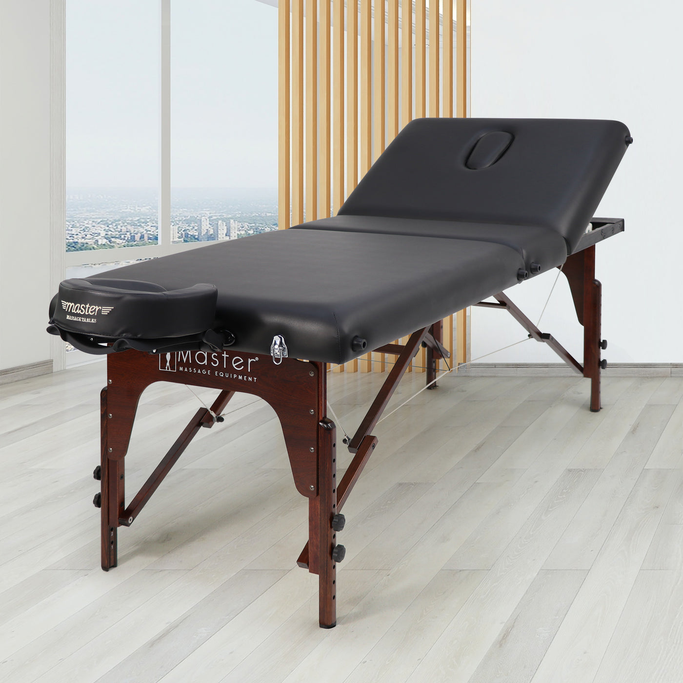 Black massage table with wooden legs on a light wood floor, brand 'Master Massage' visible.