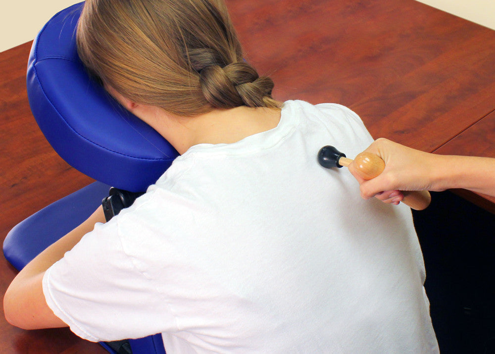 Person receiving a neck massage from a Master Massage Wooden Thumb Saver on a wooden floor.