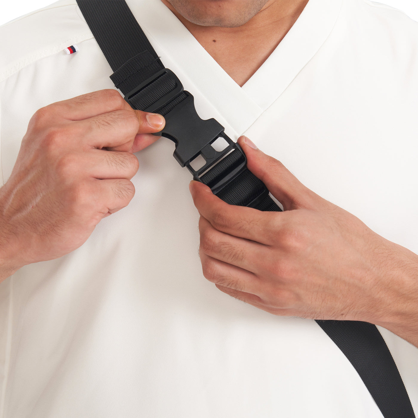 Person adjusting a black belt on a white shirt with a visible brand logo.