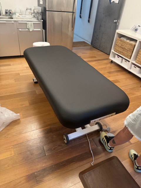 EarthLite ELLORA LIFT Massage Table in a clean room with wood floors and kitchen appliances.