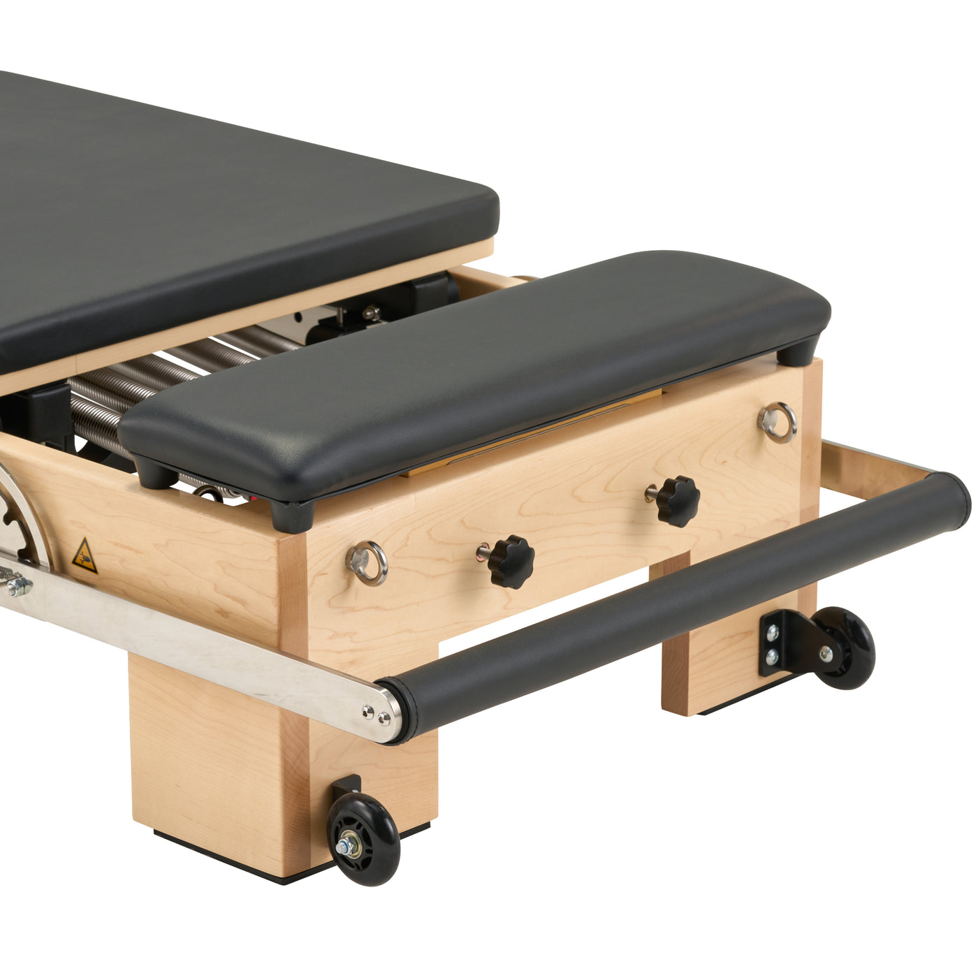 Close-up of a Pilates reformer machine showing the wooden frame, black padded footboard, metal springs, and caster wheels on a white background.