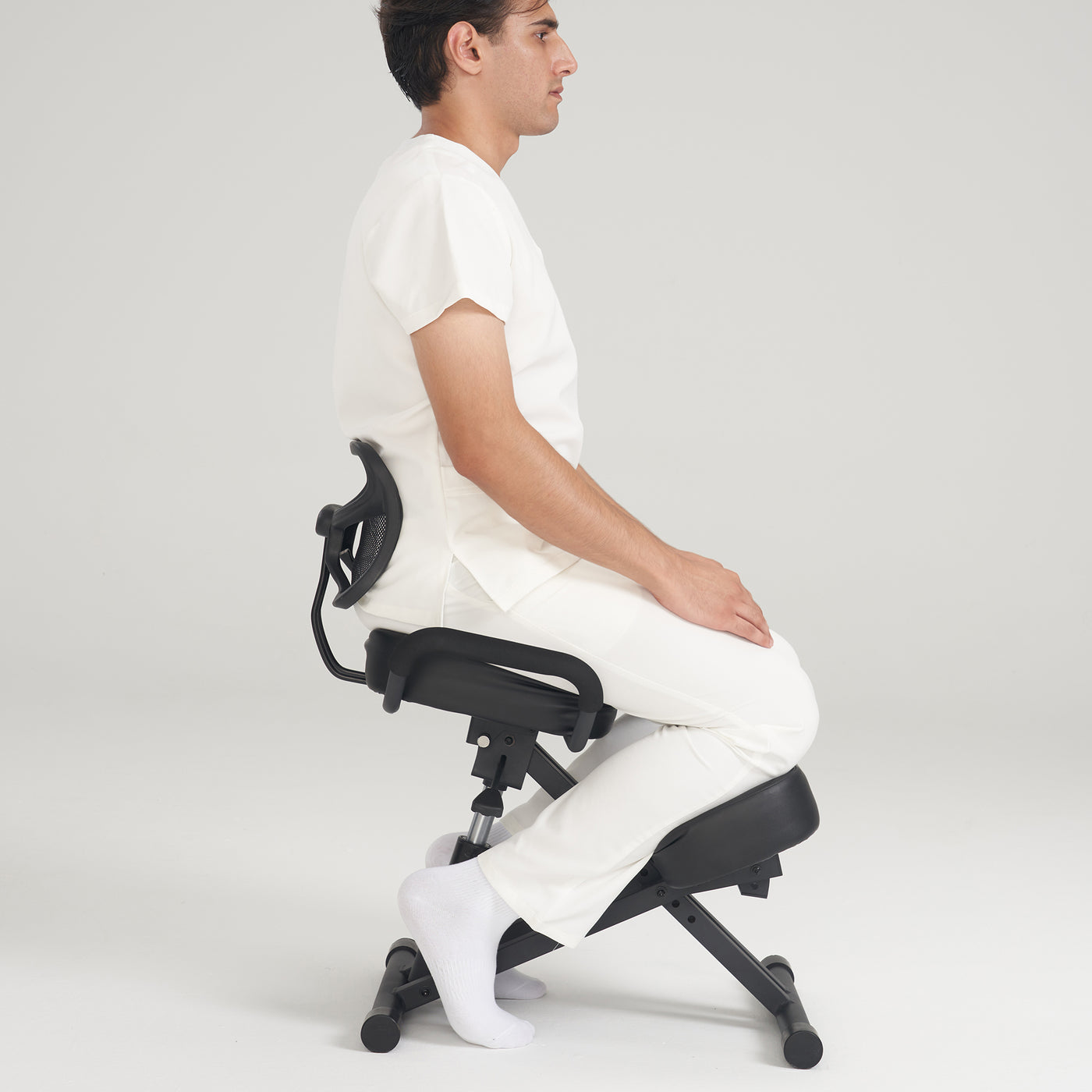 Man seated on Master Massage Ergonomic Kneeling Chair with back support against plain background.