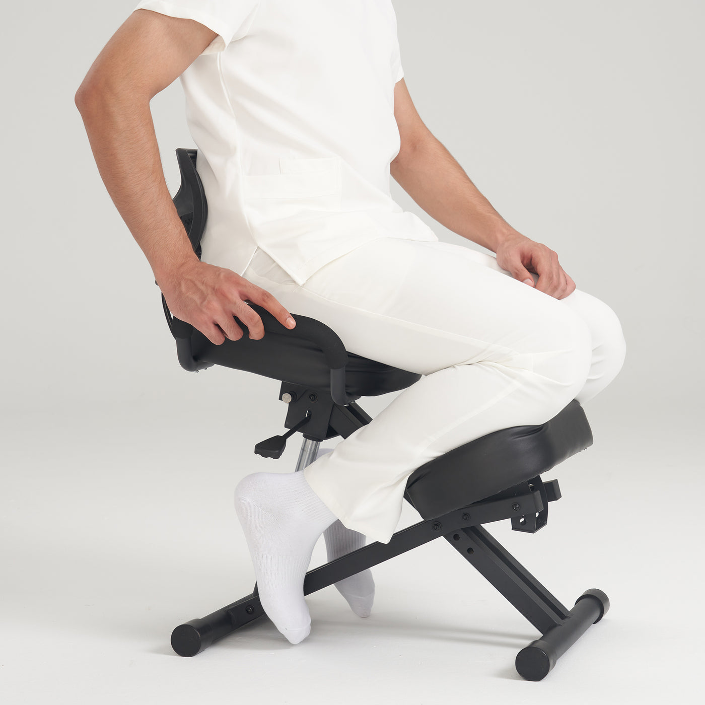 Person sitting on a Master Massage Ergonomic Kneeling Chair, wearing white clothing and socks.