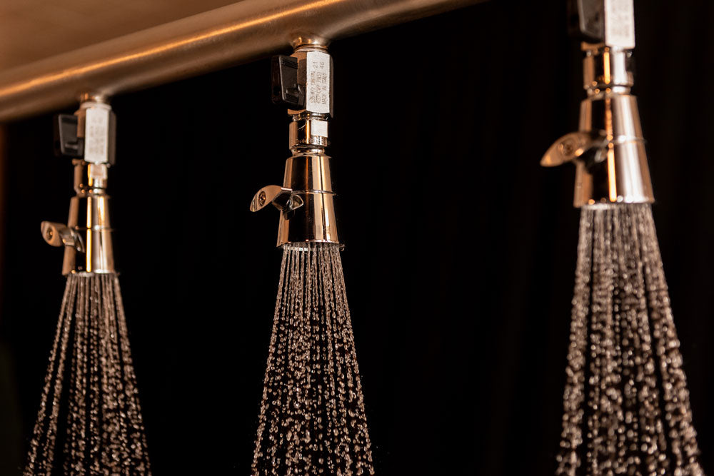 Three shower heads with water flowing against a dark background