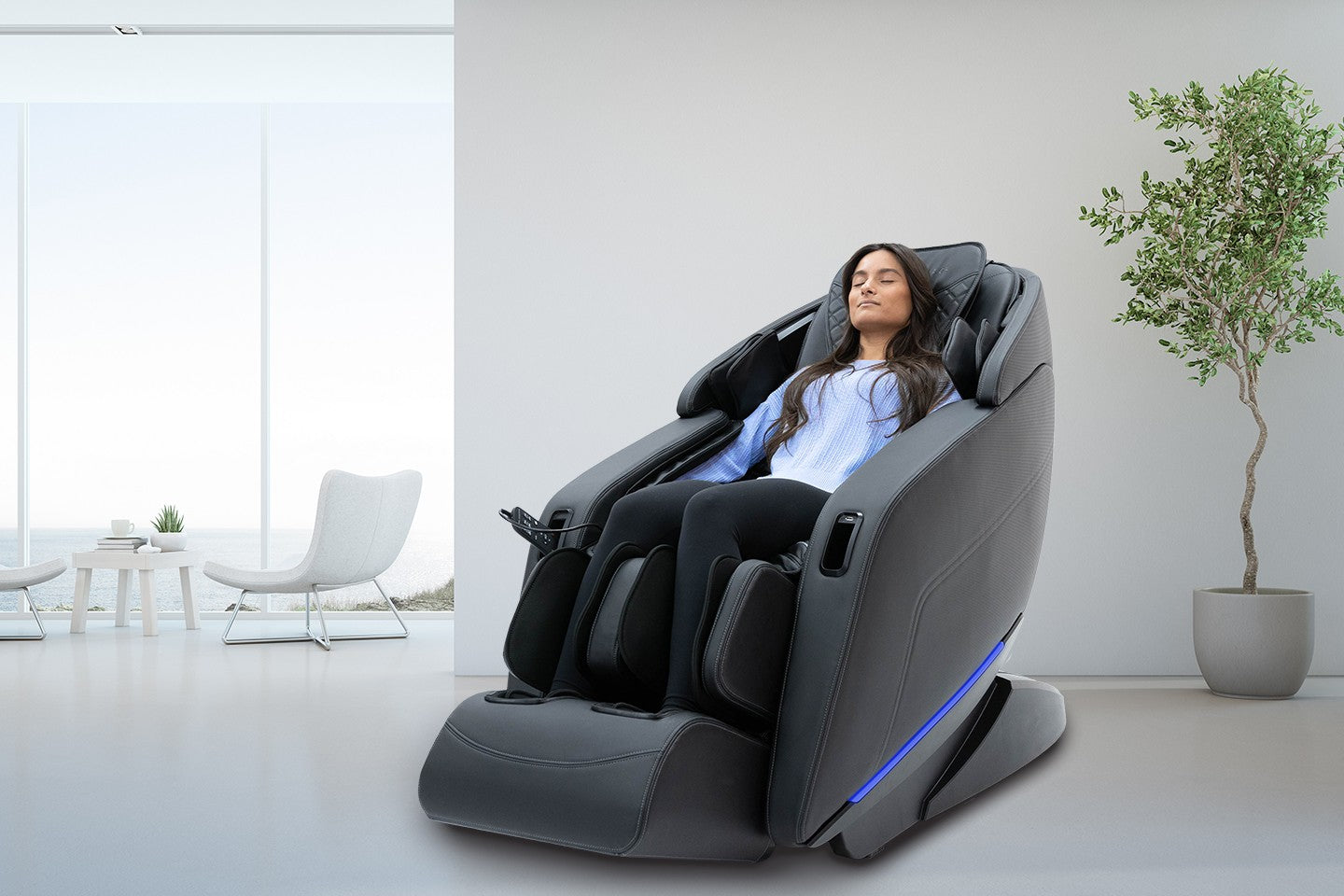 Woman relaxing in a Sharper Image Axis 4D Massage Chair in a modern room with a nearby plant.