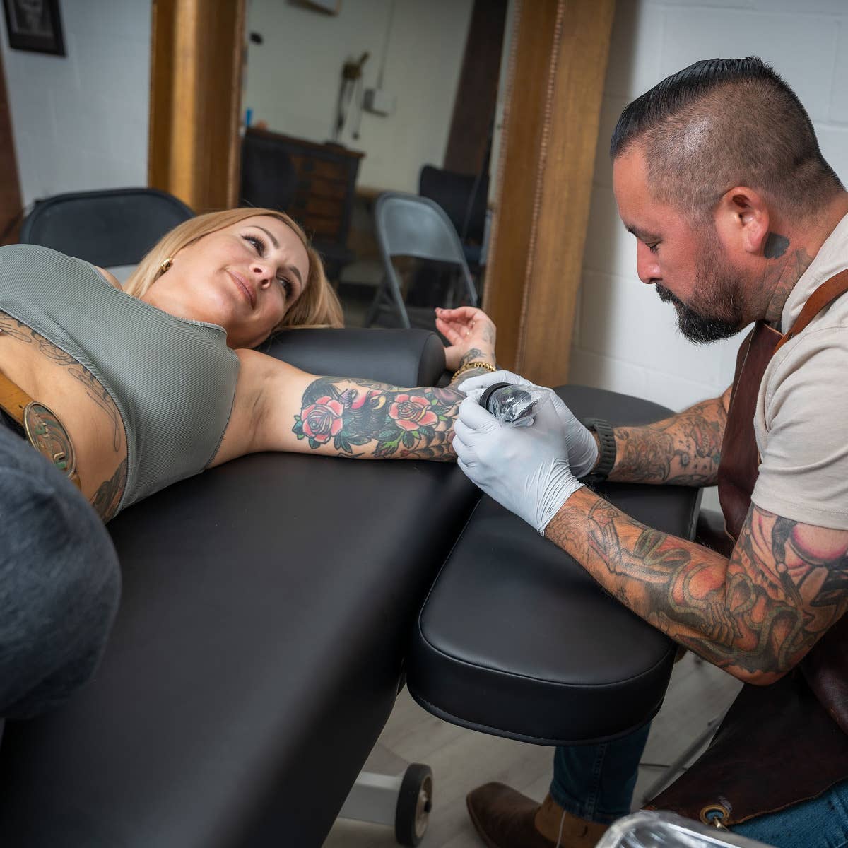 Tattoo artist works on a client relaxing on the EarthLite HYDRA Lift Tattoo Table by EarthLite.