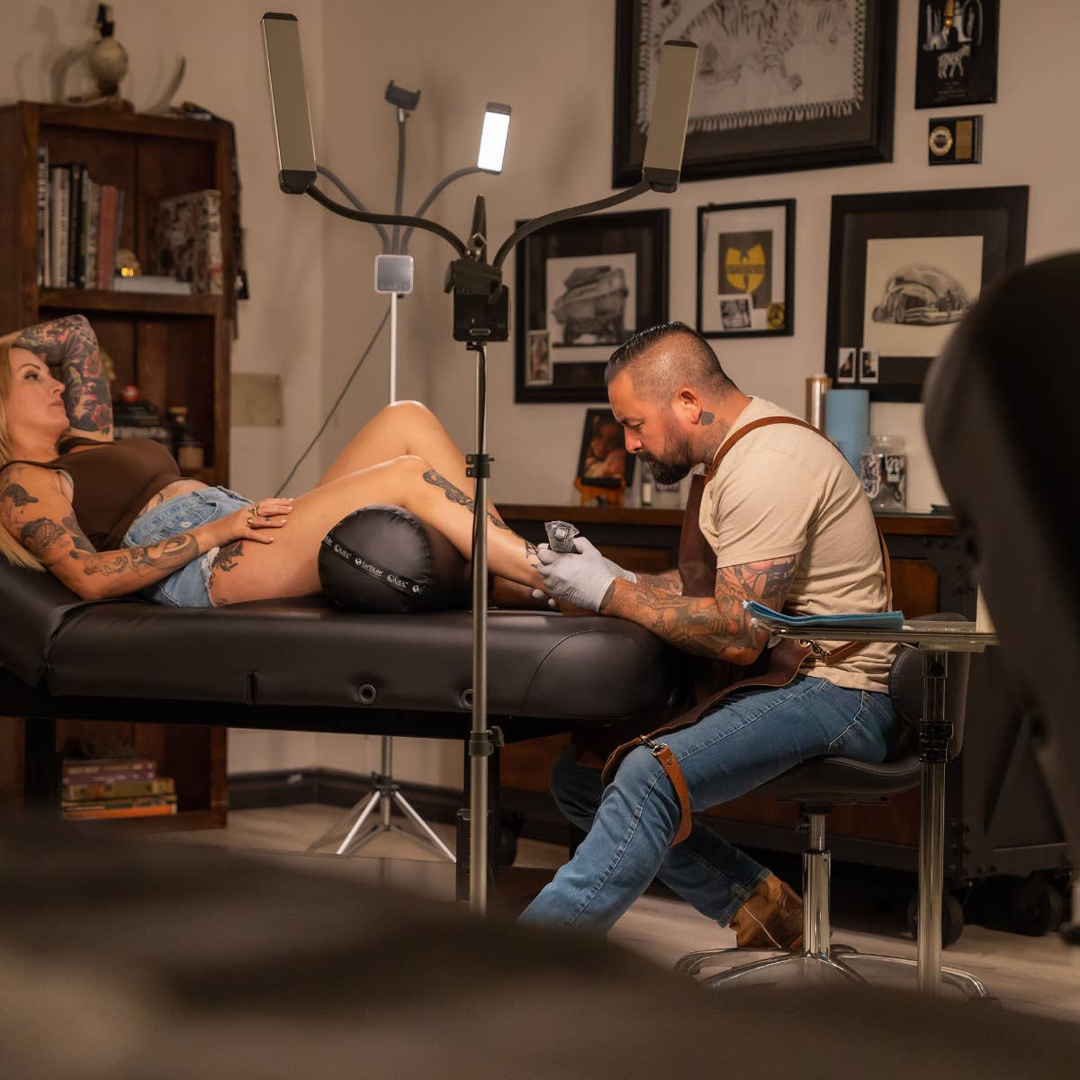 Tattoo artist works on a client's leg atop an EarthLite HYDRA Stationary Tattoo Table.