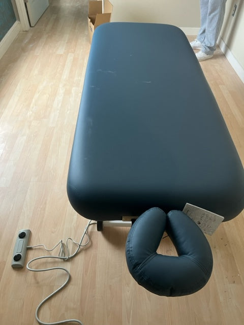 An EarthLite Ellora Lift black electric massage table with headrest sits on a wooden floor.