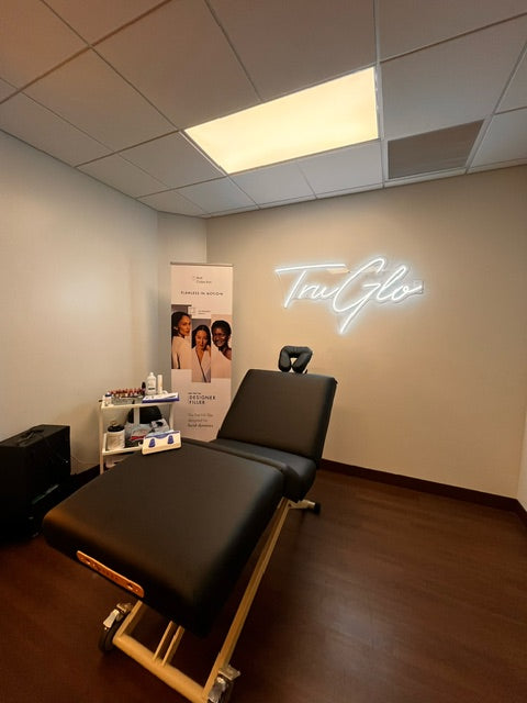 A treatment room with a Sierra Comfort electric lift table, skincare products, and a "TruGlo" sign.