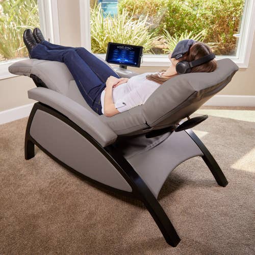 Person relaxing on Living Earth Crafts Mind-Sync 2.0™ Lounger with headphones and eye mask by windows.