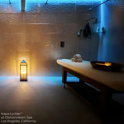 Dim spa room with Living Earth Crafts NAPA LA MER teak hydraulic table, lantern, towels, bowl.