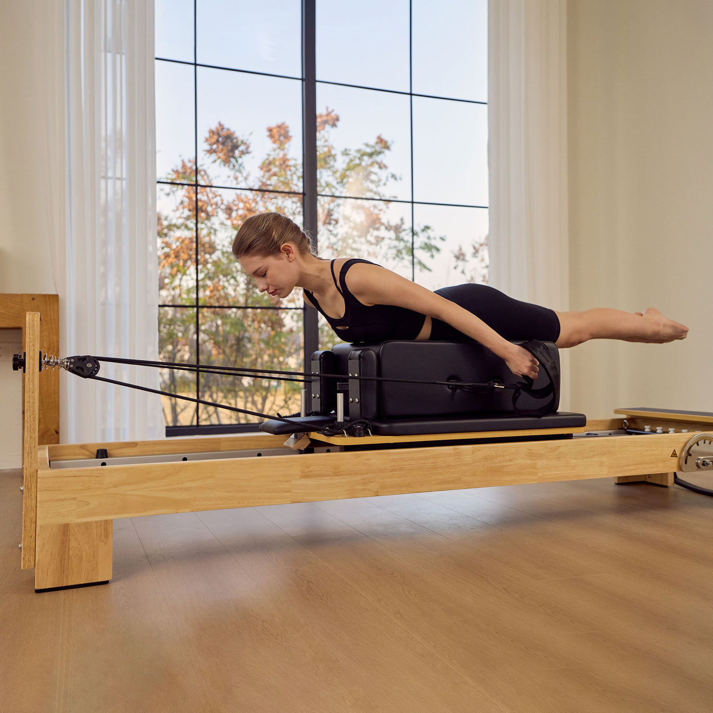 A woman in a black sports bra and leggings performs a pilates exercise on a Master Massage StudioSolid Stationary Pilates Reformer