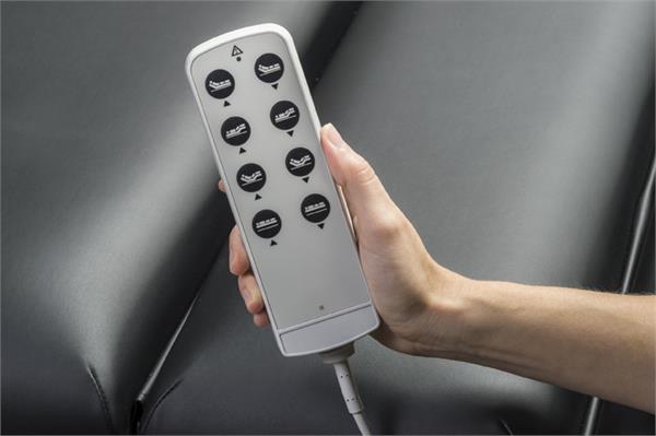A hand holds a wired remote over a Nirvana Salon Top Electric Massage Table's dark, padded surface.
