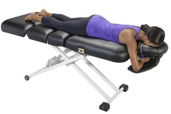 Person lying face down on a Nirvana Salon Top Electric Massage Table, wearing workout clothes.