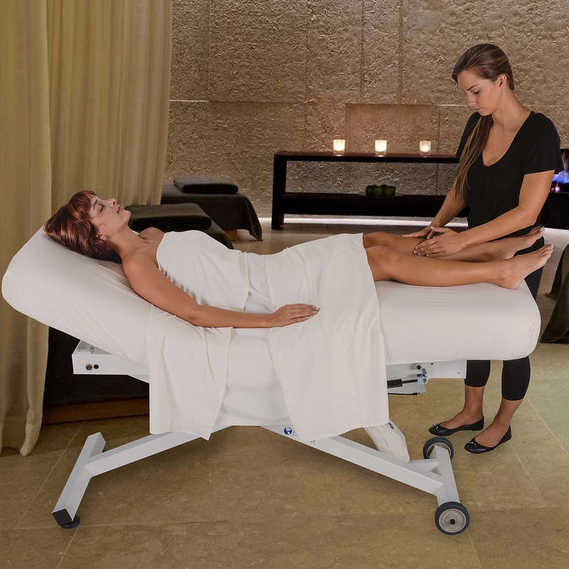 A woman gets a leg massage on an EarthLite ELLORA TILT Mobile Massage Table in a spa room.