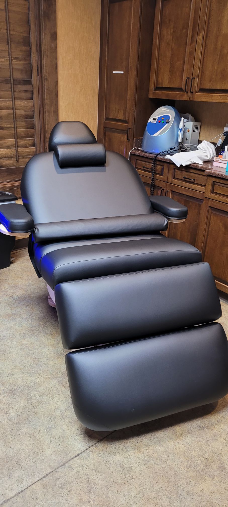 A black Living Earth Crafts CLOUD 9 spa table with memory foam in a clinic with wooden cabinets.