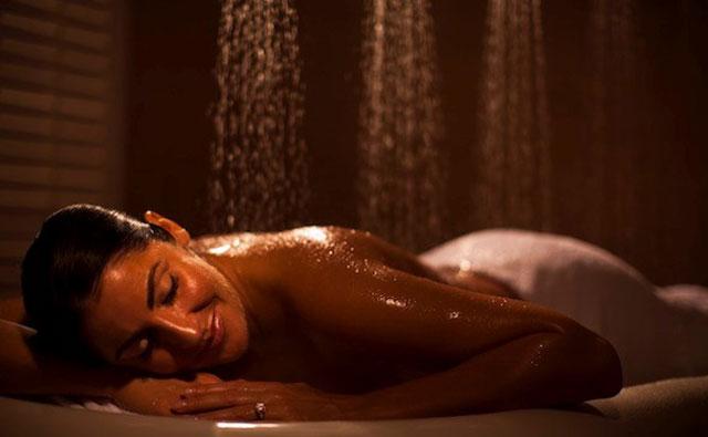 A woman relaxes under the Water Werks Typhoon 7 Head Vichy Shower, eyes closed in bliss.